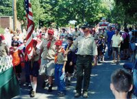A giant American flag being being held up my multiple scouts, who surround it.  They are all marching forward.