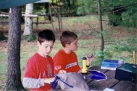 Two scouts are sitting at a picnic table.  The one on the right is looking at a compass.