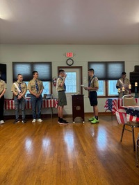 Five people in Class A uniforms.  The two in the middle are facing each other, and the one on the left is giving the scout sign.