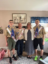 Four people standing in their living room facing the camera.  Three are in class A uniforms.