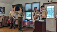 Four people stand in front of a room behind a podium.  Ben is giving the scout sign.