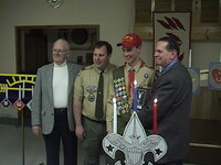 Four people smiling at the camera.  The two in the middle are wearing Class A uniforms.