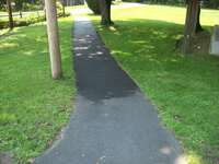 A paved path going down the middle of some grass.  To the left is a telephone pole.