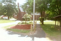 A chain railing to the left of a path.  To the left is a garden with a red tree in it.