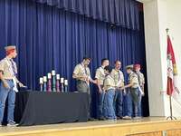 The scoutmaster giving an award to two scouts.  He is joined by other adults and scouts standing beside him.