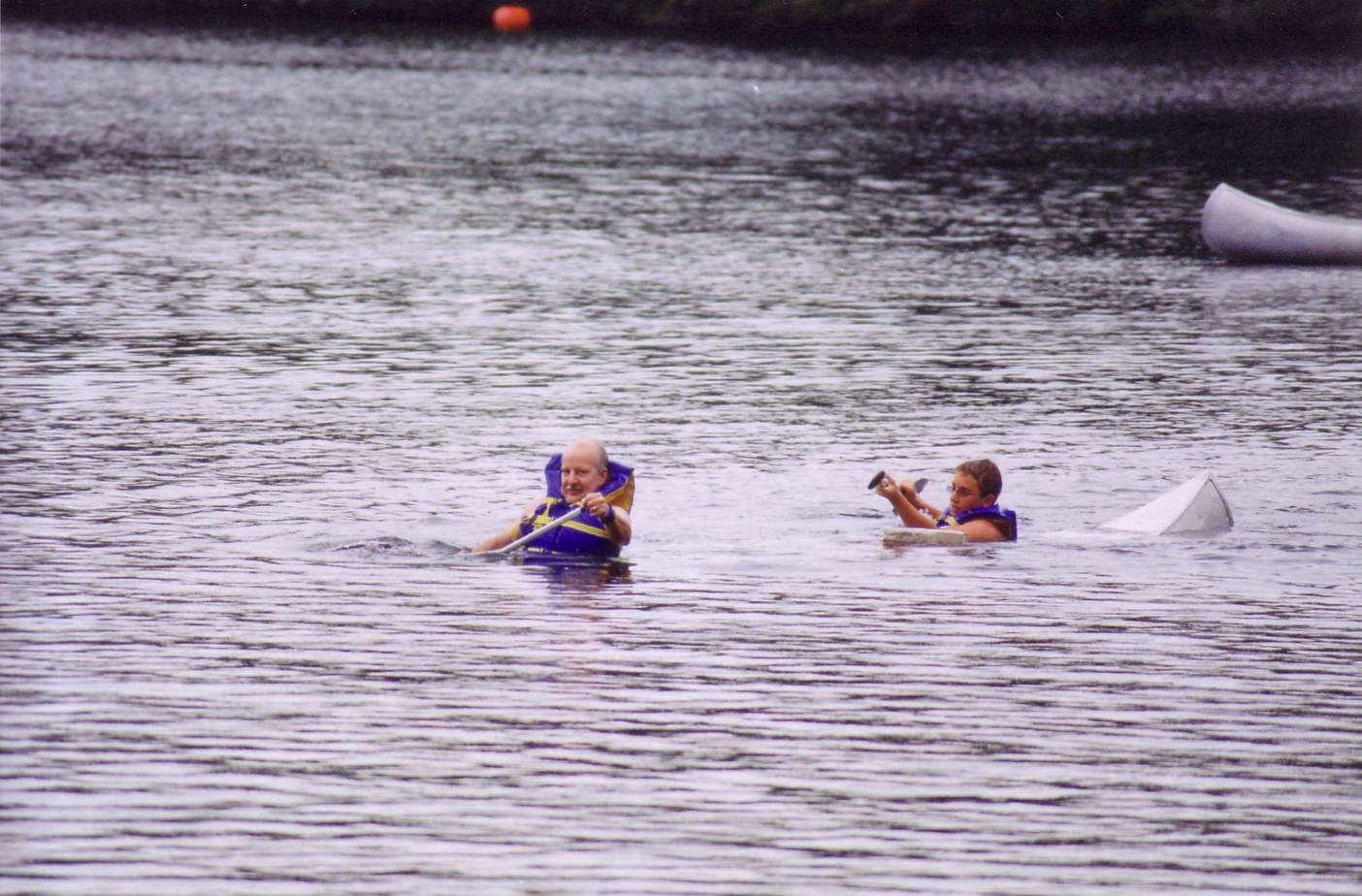 Two people in a canoe that has been swamped.  The canoe is just under the water surface.
