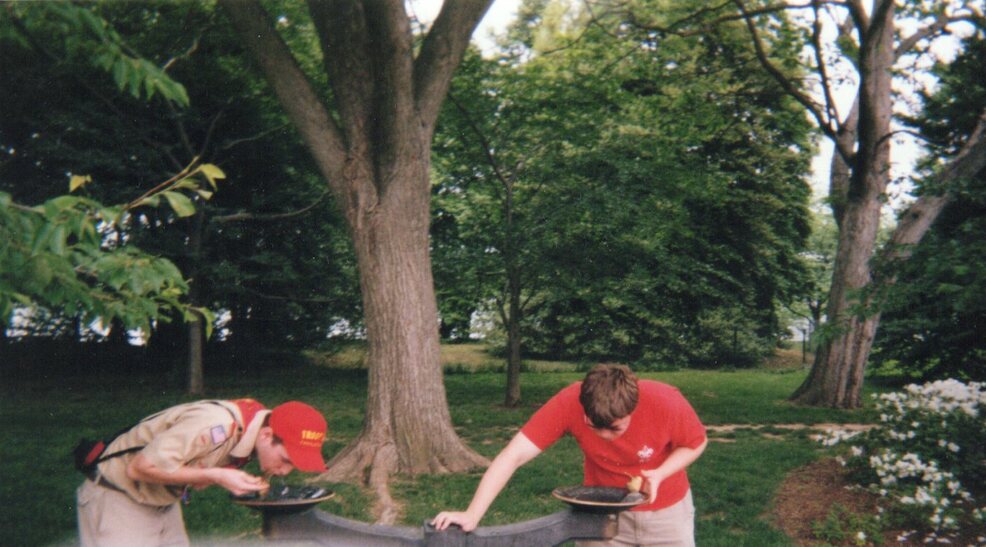 Two scouts taking a drink from water fountains.