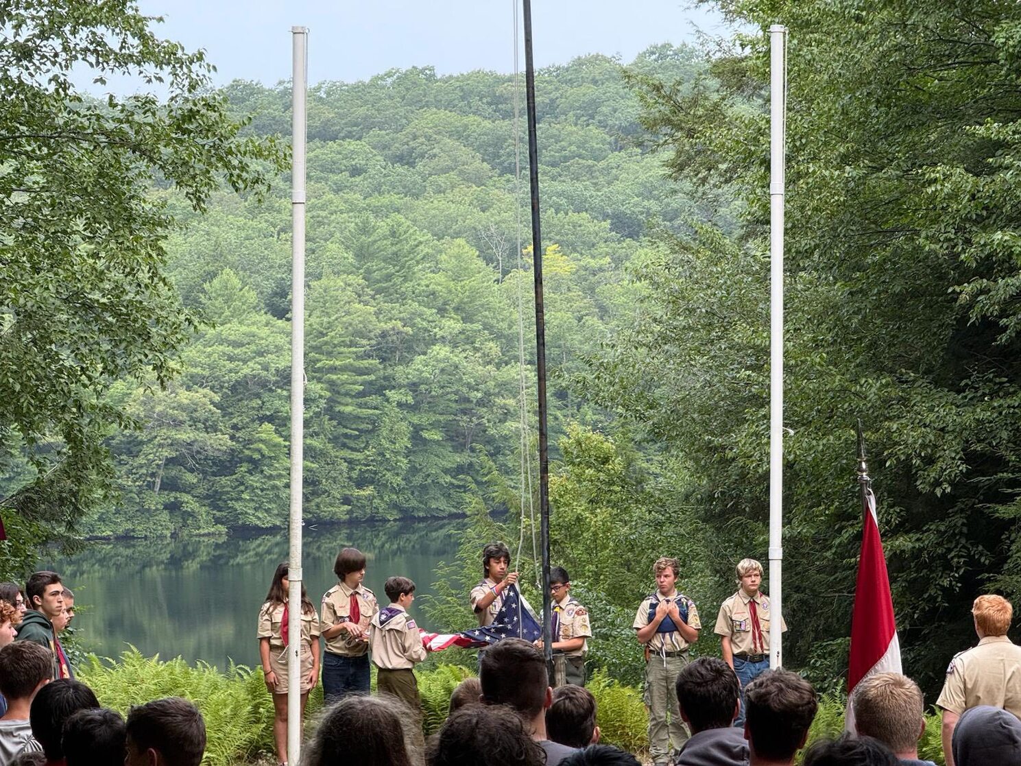 Seven scouts in class A uniforms performing a flag ceremony.  Three scouts are holding the American flag at the center pole.  The other four scouts are standing to the right and left of them at attention.