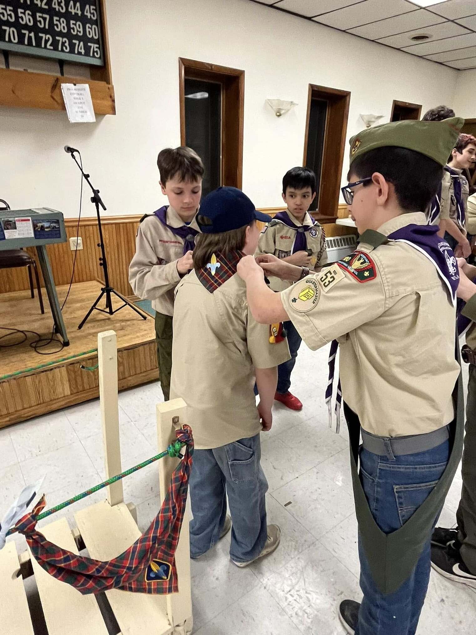 Two scouts are reaching over to help remove the Webelos neckerchief off of a Cub Scout.