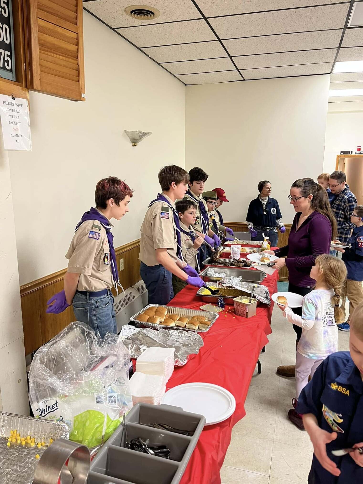 Six scouts help serve dinner.  All are wearing class A's and wearing purple gloves.