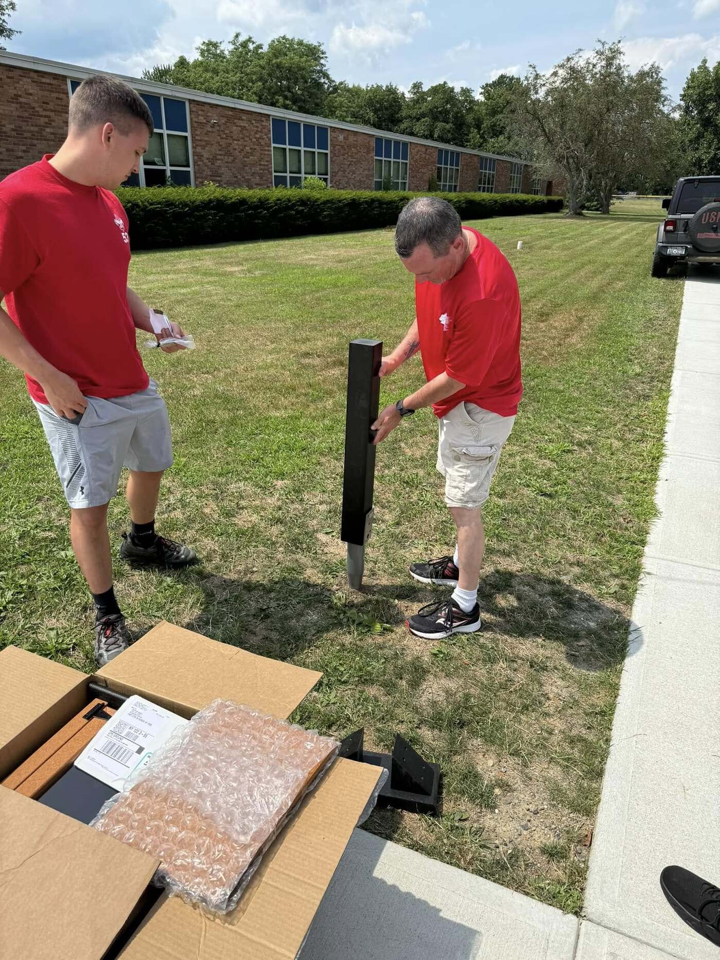 One person is holding the post in the ground, other looks at it to the side.