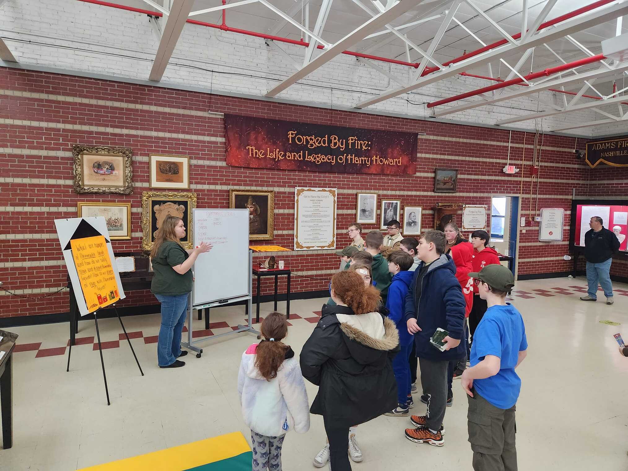 A group of scouts standing looking towards a woman writing something on a whiteboard on wheels.