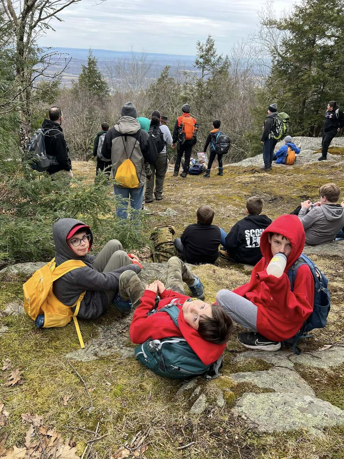 Three scouts look at the camera while behind them is the cliffs at Rotary.  A group of others looks over the cliff.