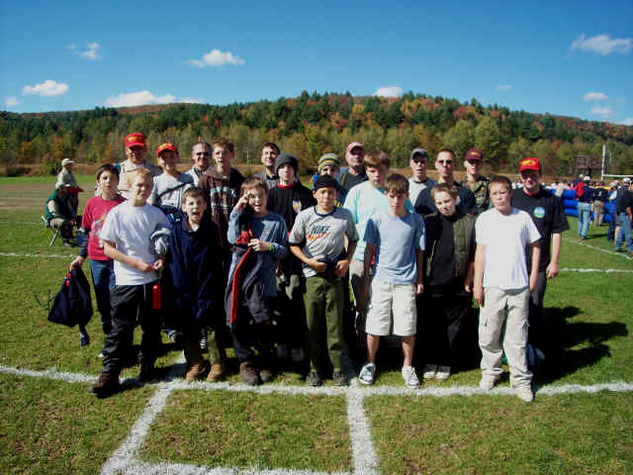 21 scouts and leaders standing on a grassy field, facing the camera.