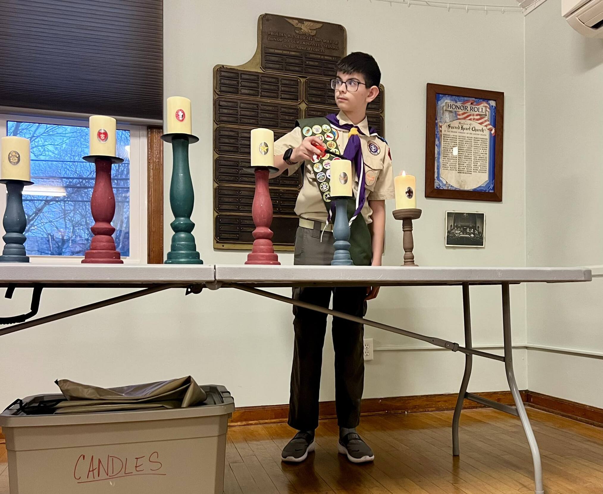 A scout in a class A lights a candle in the front of the room.