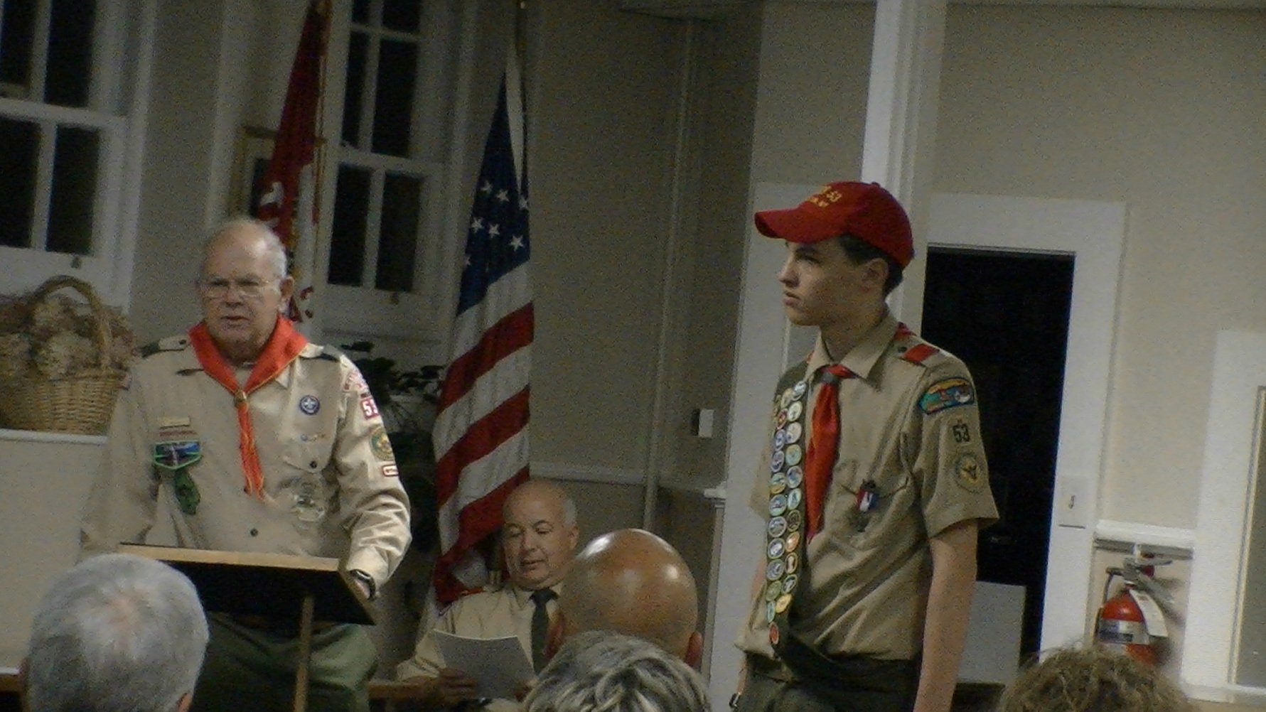 Two people standing in Class A uniforms.  The person on the left if at a podium, reading from something on it.