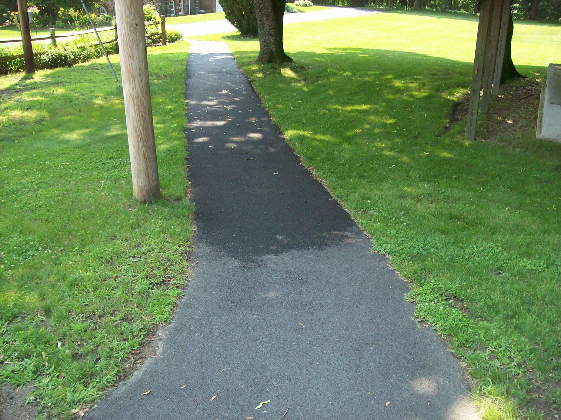 A paved path going down the middle of some grass.  To the left is a telephone pole.