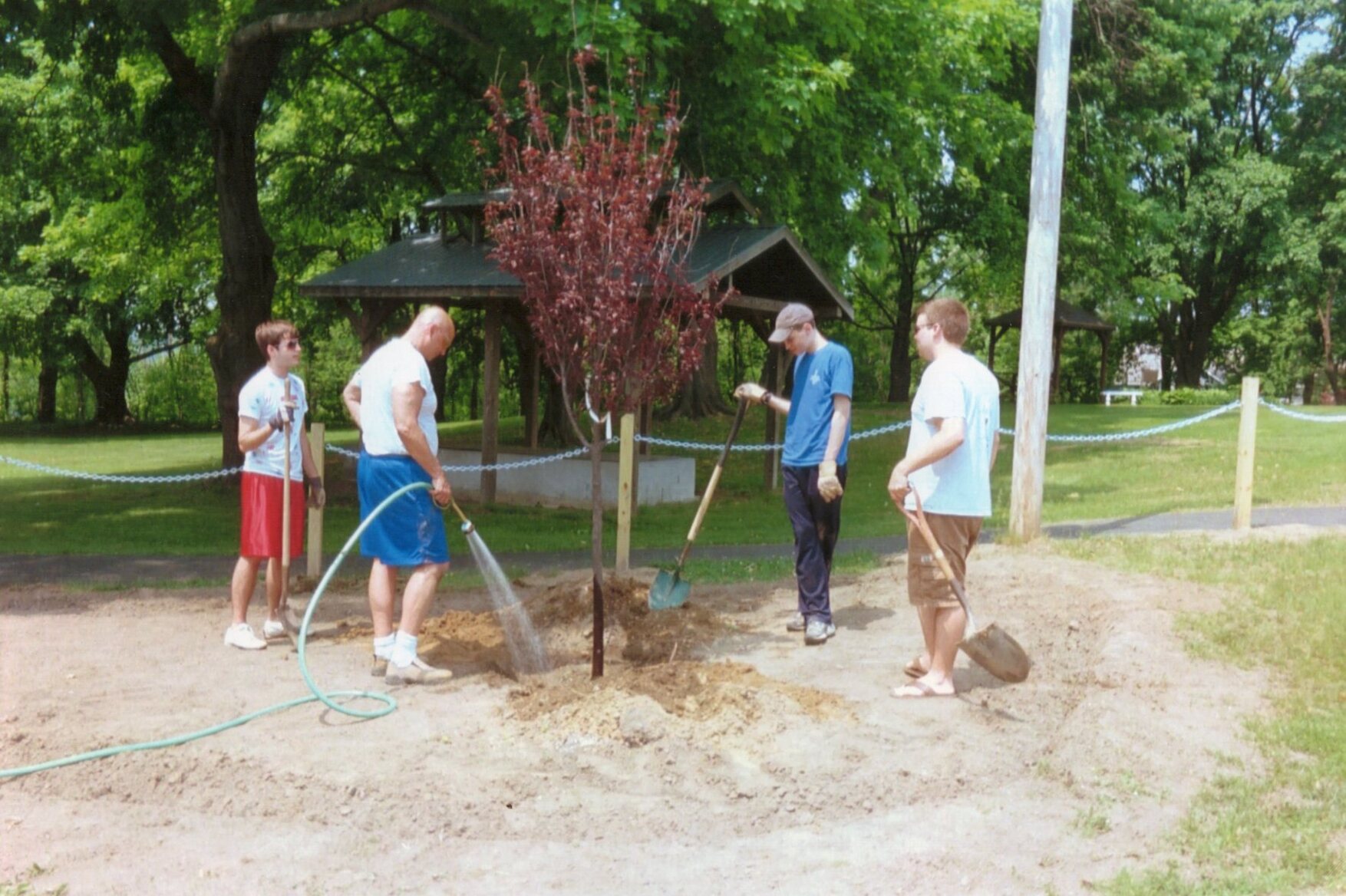 Seth's dad filling the hole we dug for the tree with water.  Brett, Rob, and Seth stand around him holding shovels waiting.
