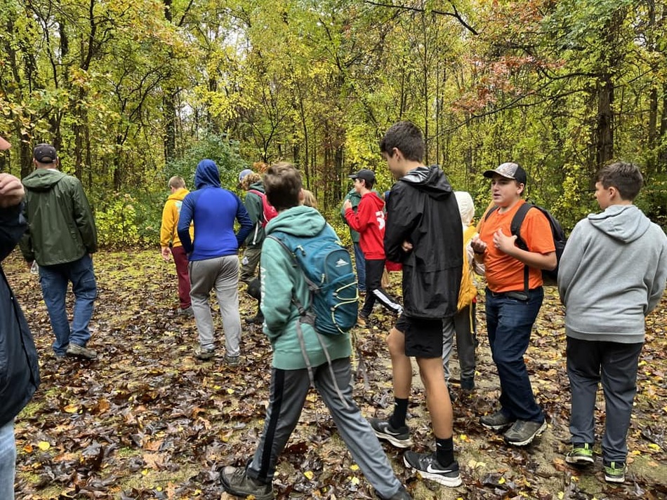 A group of scouts walking away from the camera on a leafy trail.